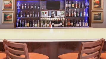 Una zona de bar con varias botellas de licor, un televisor y obras de arte enmarcadas en las paredes.