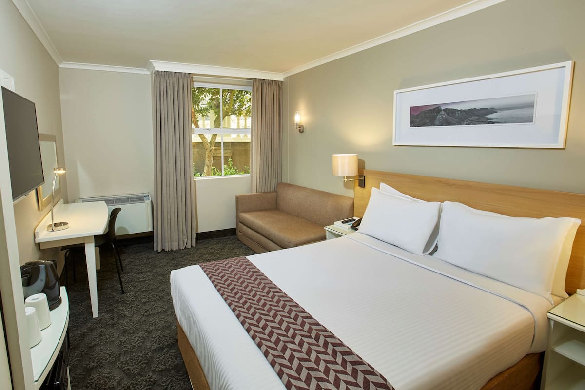 Una habitación de hotel con cama, escritorio, silla, sofá y ventana con cortinas.