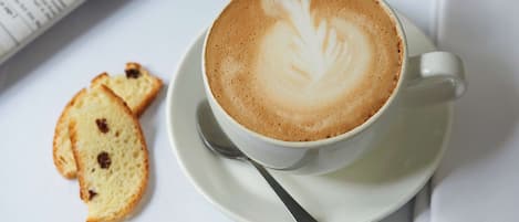 Una taza de café con diseño de leche, sobre un platito, acompañada de una cuchara y dos rebanadas de tostada.