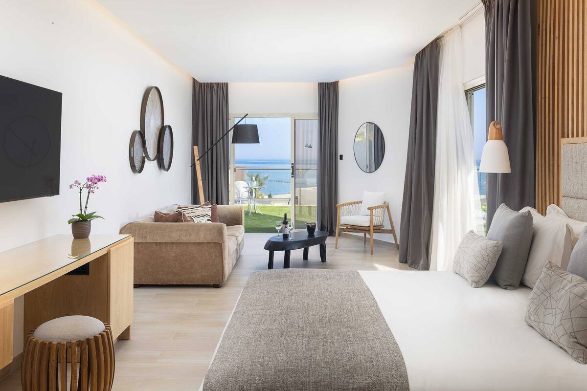Een moderne hotelkamer met een groot bed, een bank, een bureau en uitzicht op zee.