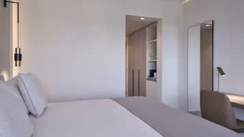 Una habitación de hotel moderna con una cama grande, una mesita de noche, una silla, un armario y un espejo.
