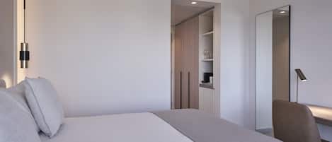 Una habitación de hotel moderna con una cama grande, una mesita de noche, una silla, un armario y un espejo.
