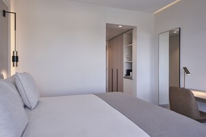 Una habitación de hotel moderna con una cama grande, una mesita de noche, una silla, un armario y un espejo.