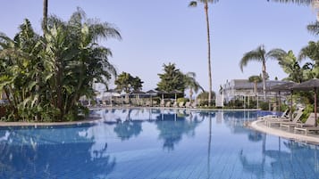 Una piscina con sillones de descanso y palmeras.