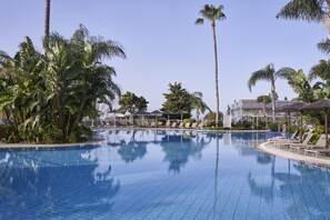 Una piscina con sillones de descanso y palmeras.
