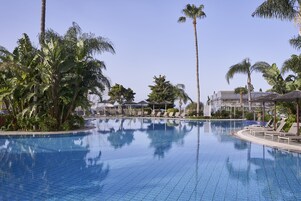 Una piscina con sillones de descanso y palmeras.