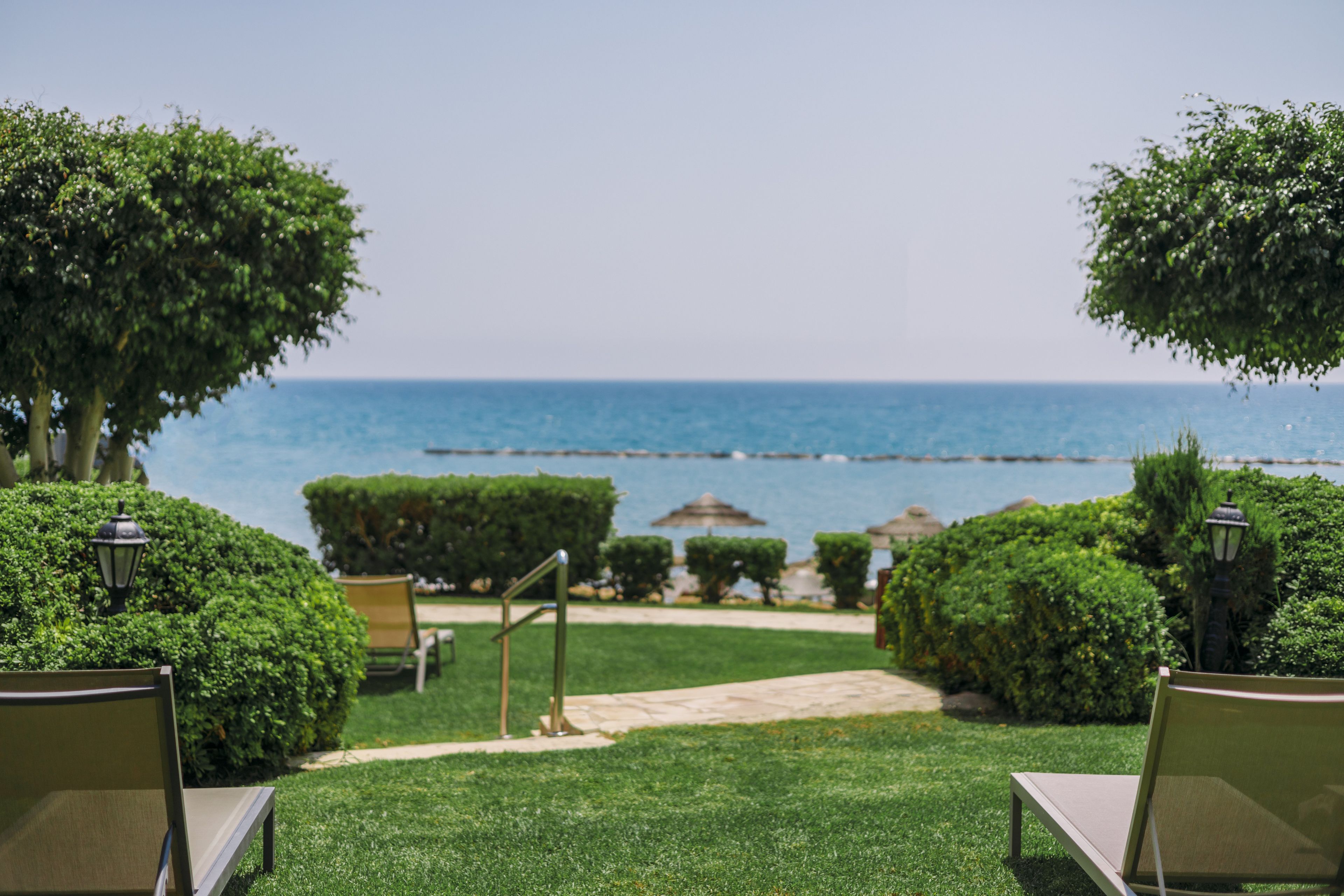 Un jardín con vistas al mar, que incluye un sendero, sillas y setos cuidados.