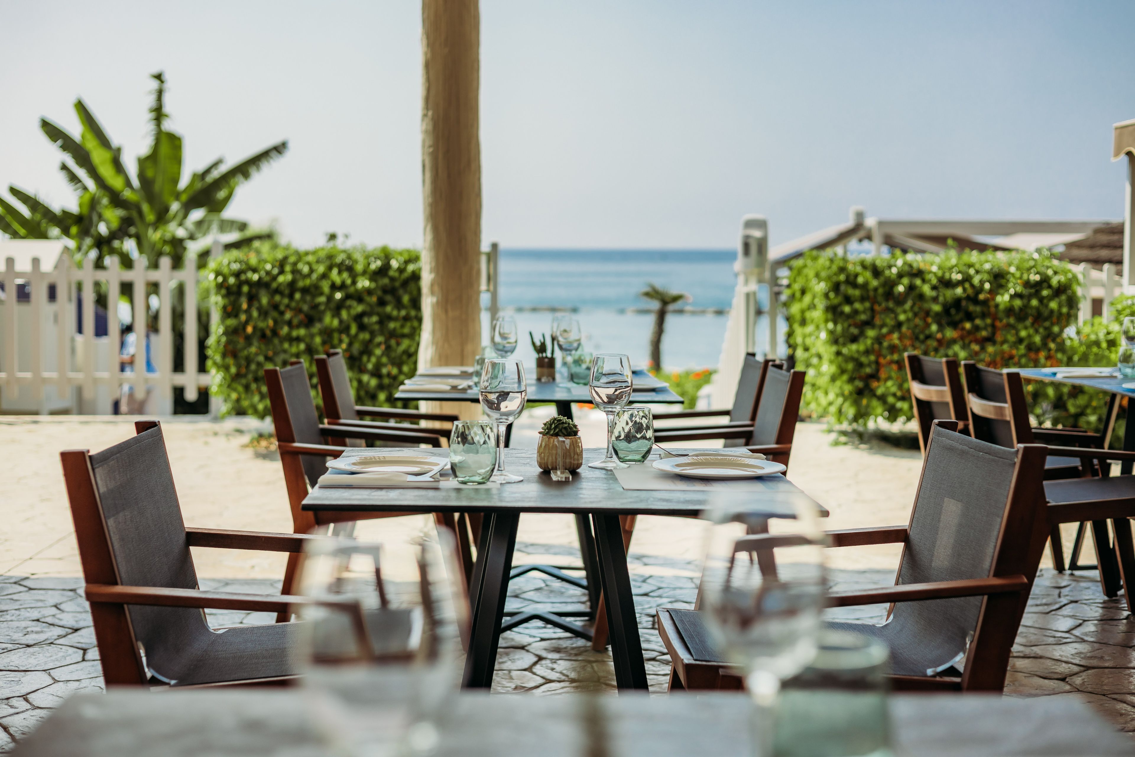 An outdoor dining area with tables set for two, overlooking a body of water.