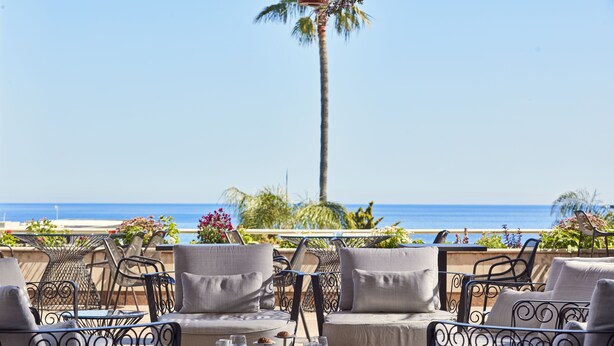 An outdoor seating area with a view of the ocean, featuring wicker chairs and a table with a tray of drinks and pastries. - Atlantica Bay Hotel - Adults Only (Limassol)