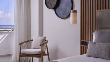 A hotel room with a bed, a chair, a wall-mounted lamp, and a view of the sea.