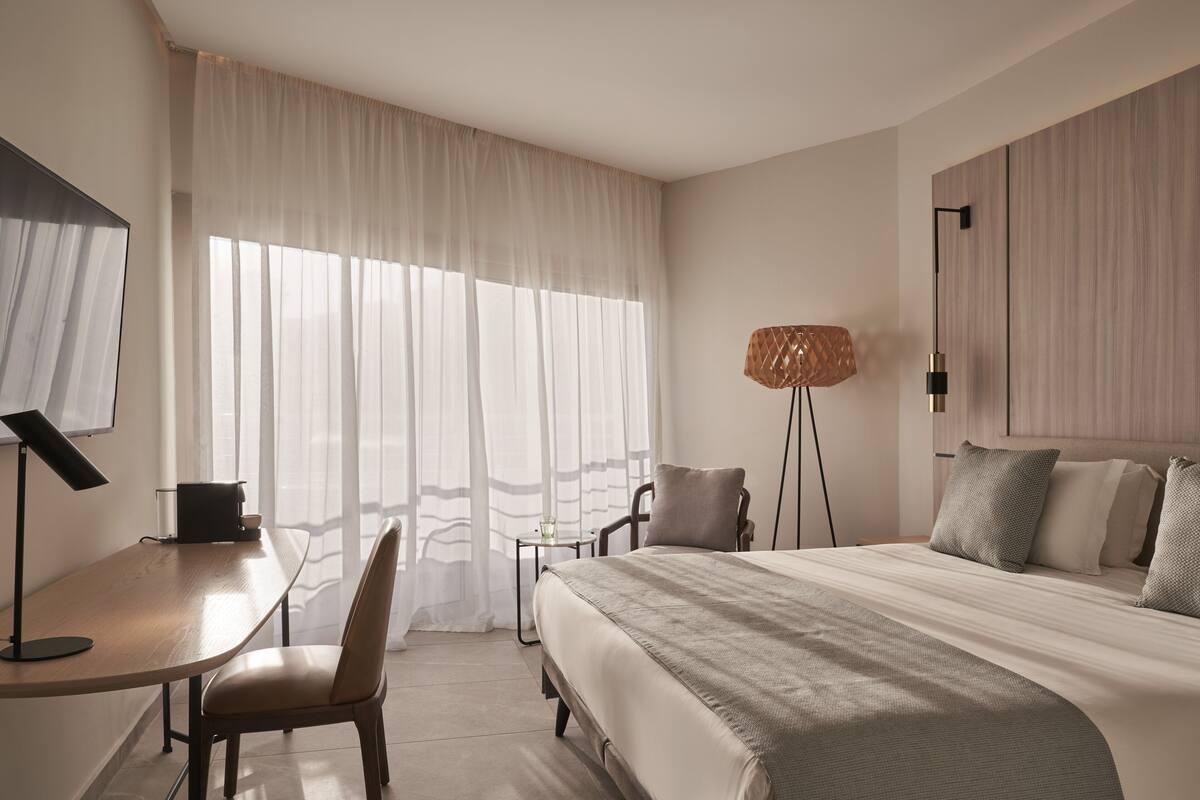 Een moderne hotelkamer met een groot bed, een bureau met lamp, een stoel en een klein tafeltje.