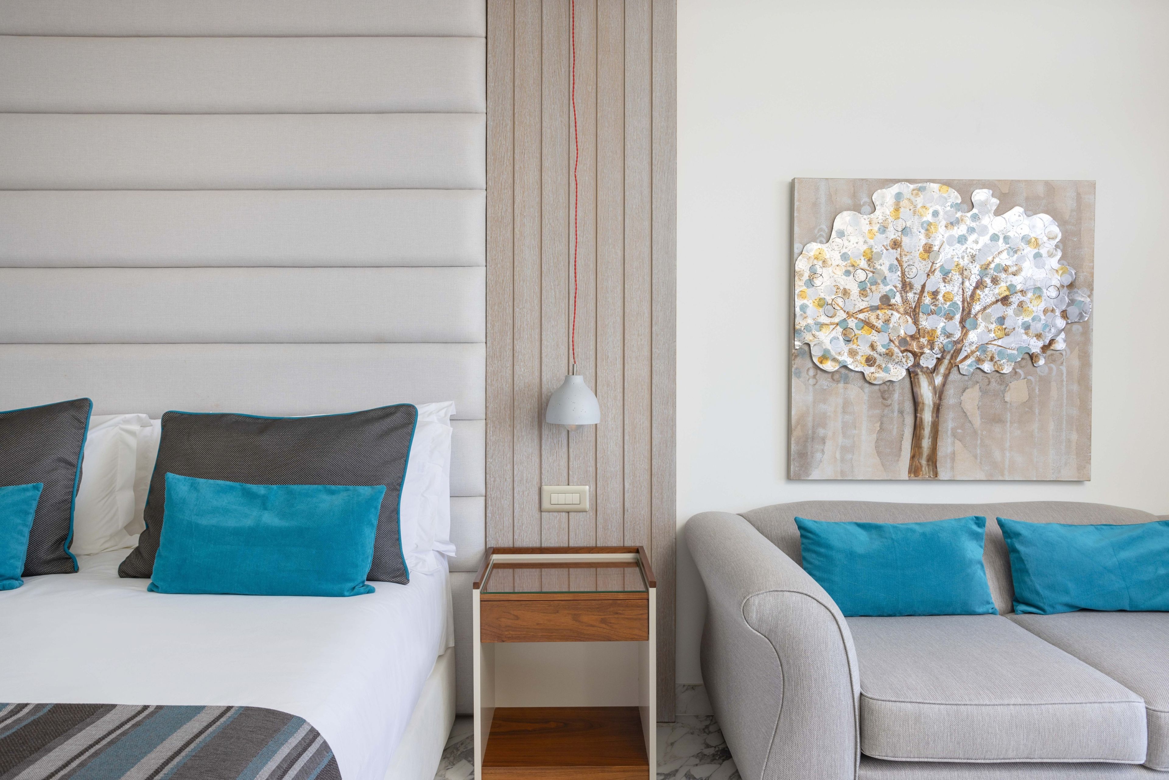 A bedroom with a bed, a nightstand, a lamp, a painting, and a sofa.