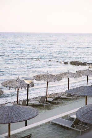 A beach with lounge chairs and thatched umbrellas, overlooking the sea.