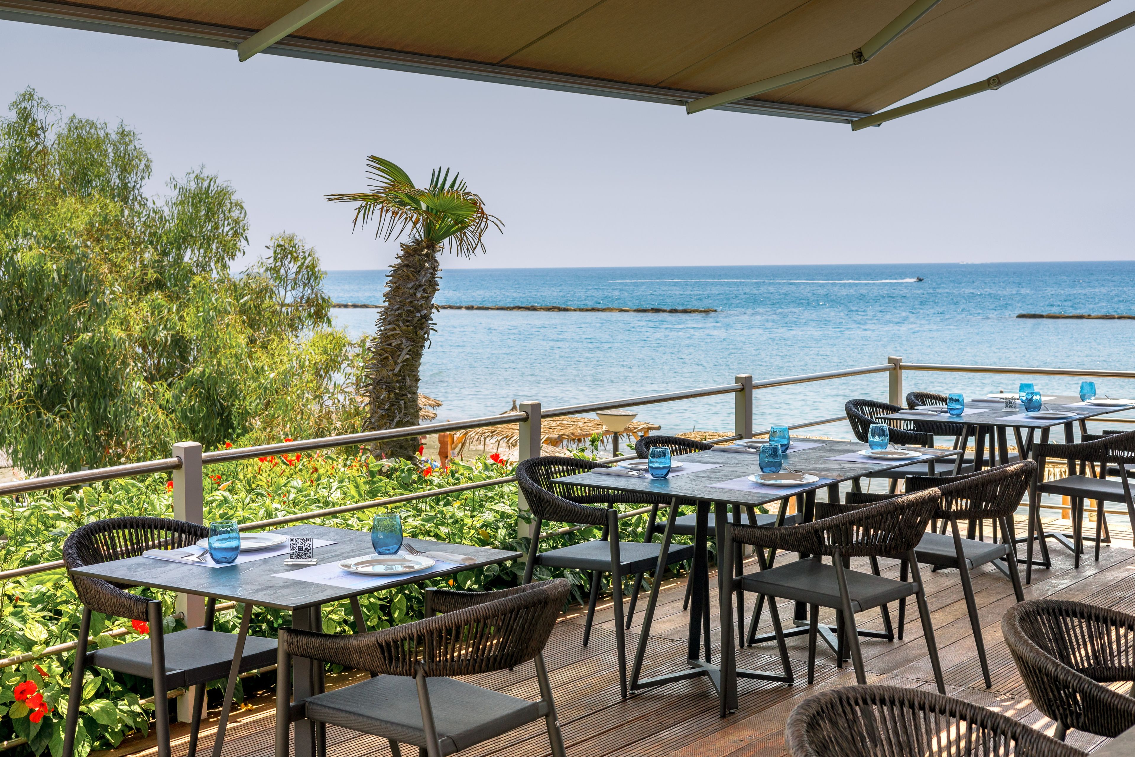 Un espace extérieur aménagé pour les repas, avec des tables et des chaises, donnant sur une étendue d’eau.