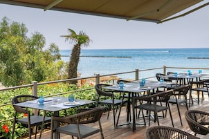 Un espacio de comedor al aire libre con mesas y sillas, con vista a un cuerpo de agua.