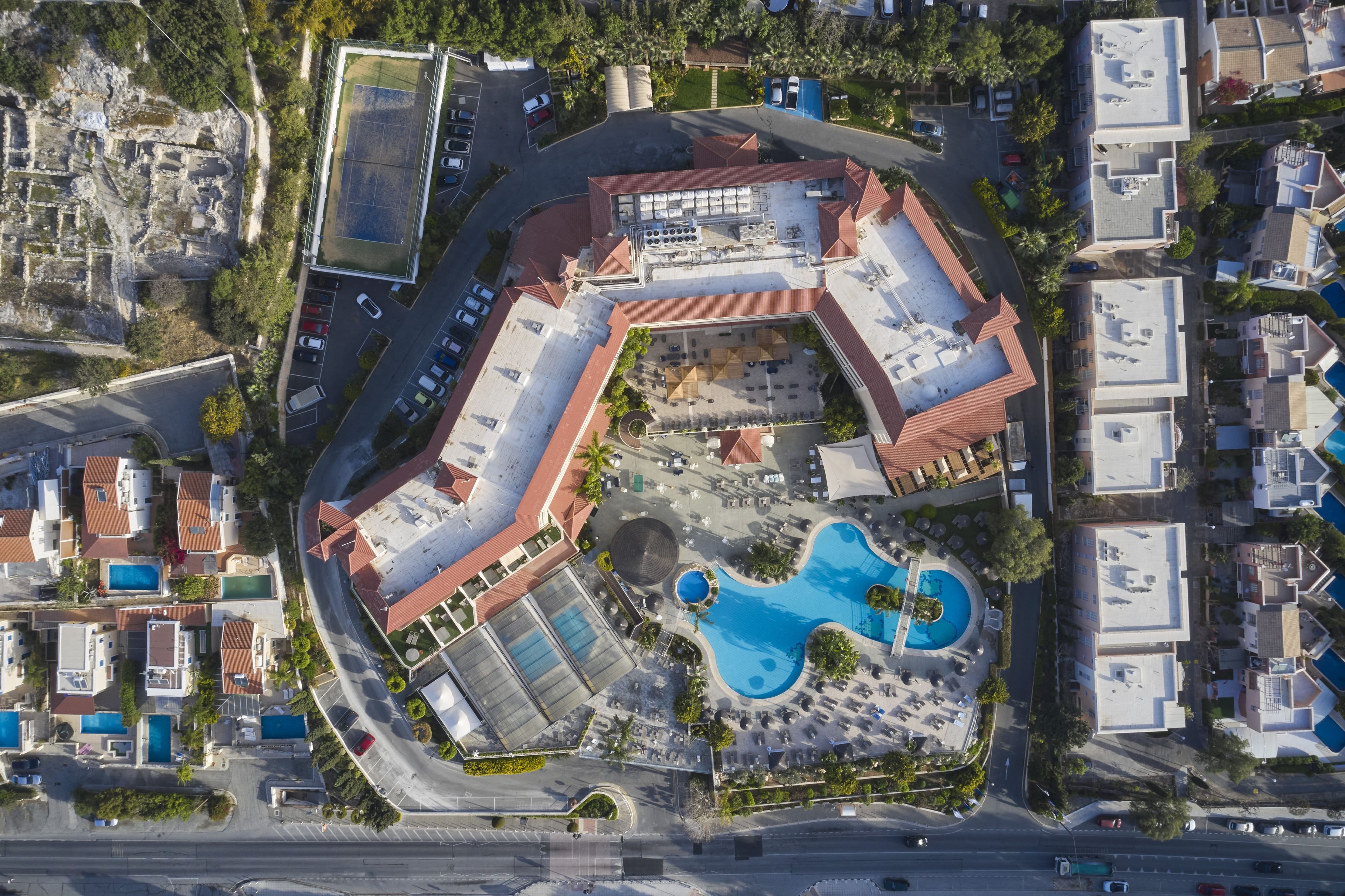 An aerial view of a resort with a swimming pool, multiple parking areas, and a mix of residential and commercial buildings.