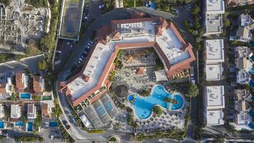 An aerial view of a resort with a swimming pool, multiple parking areas, and a mix of residential and commercial buildings.