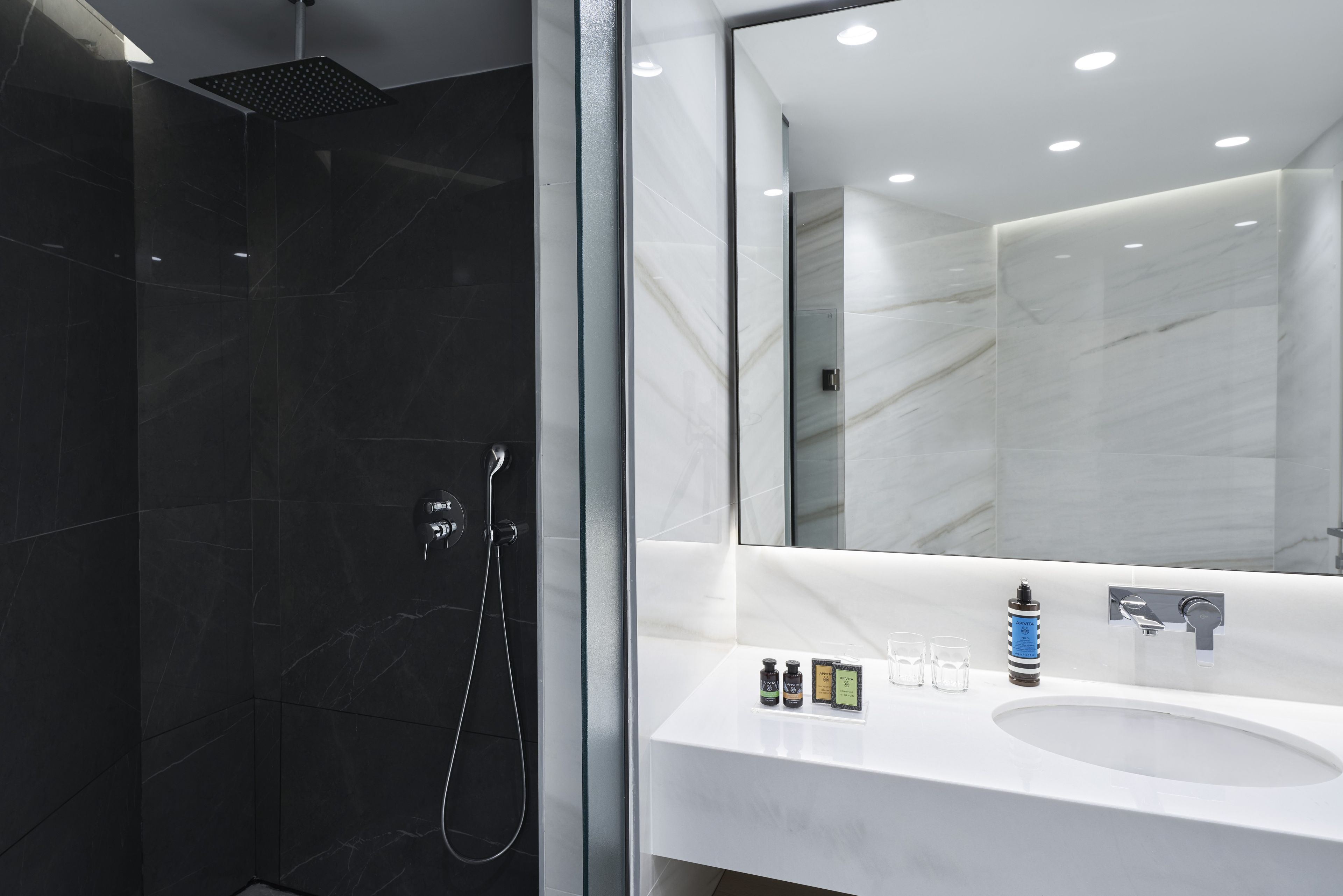 A modern bathroom with a glass-enclosed shower, a large mirror, and a white sink with toiletries.