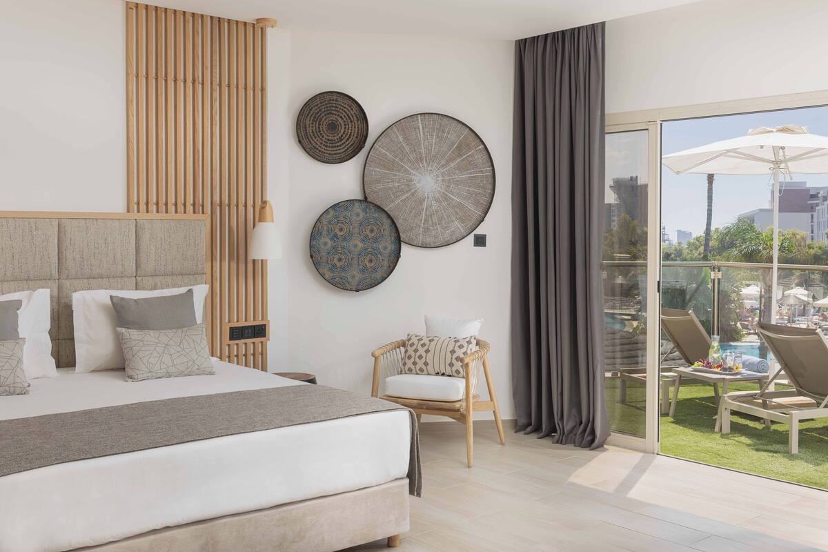 Een moderne hotelkamer met een groot bed, een wand van houten latten en een balkon met zitplaatsen.