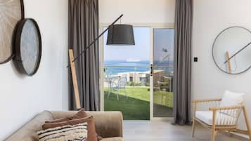 A modern living room with a sofa, a chair, a large window with curtains, a wall clock, and a view of the ocean.