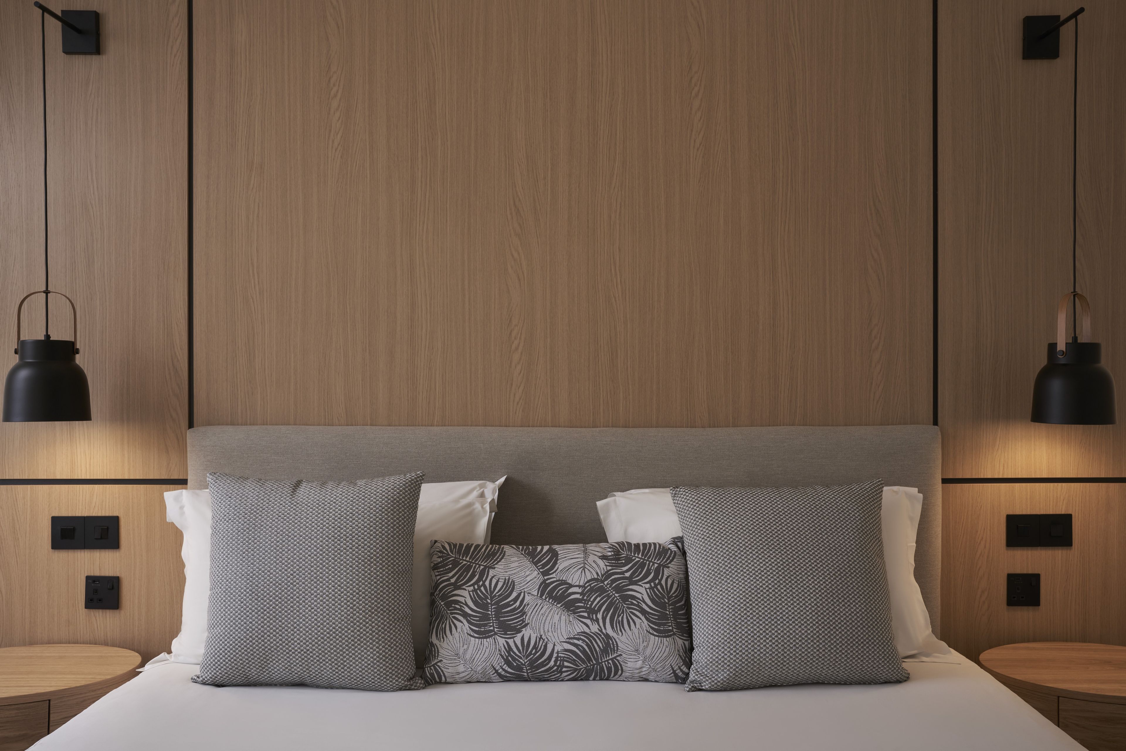 A bedroom with a wooden headboard, two bedside tables, and a bed with patterned pillows.