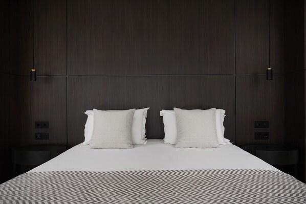 A modern hotel room with a large bed, two bedside tables, and a patterned rug.