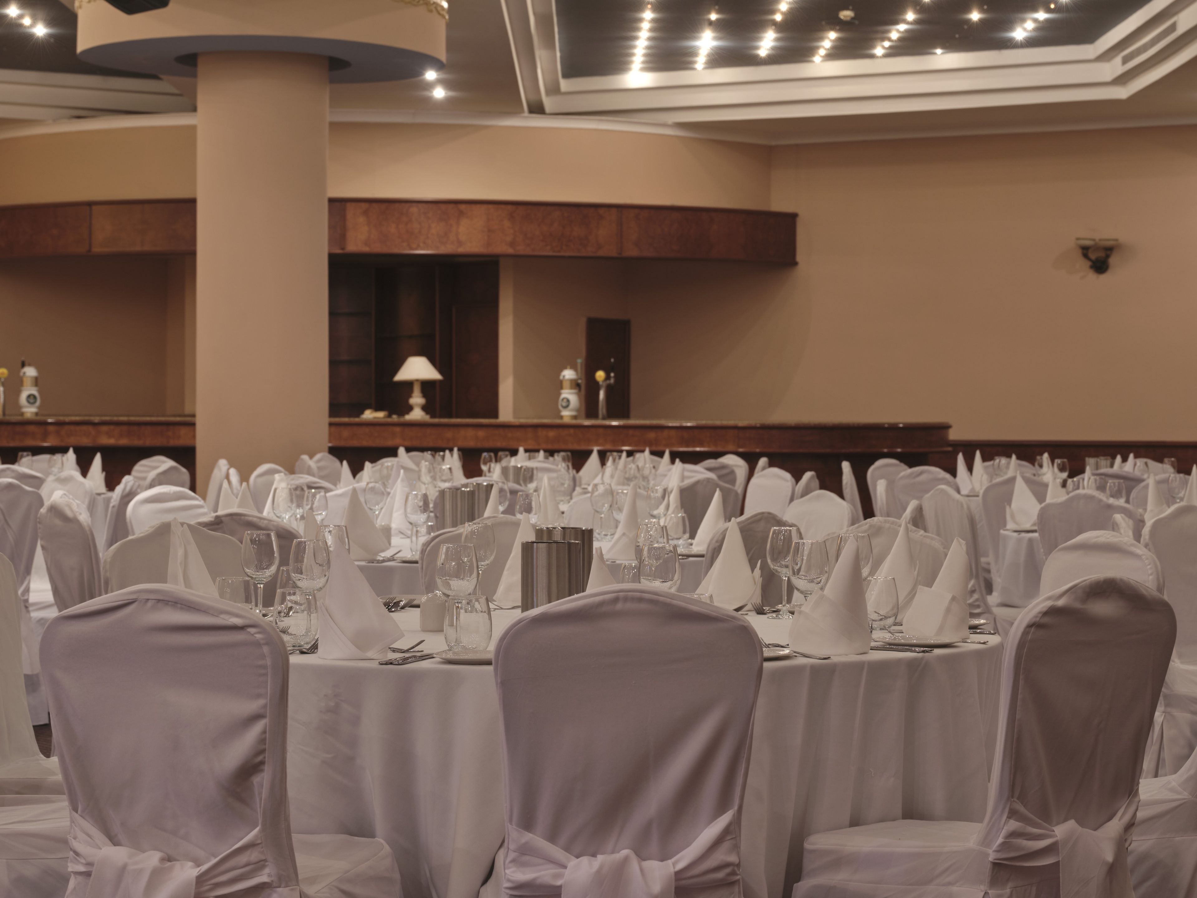 Un salón de banquetes con mesas redondas cubiertas con manteles blancos, cada una con cristalería y cubertería.