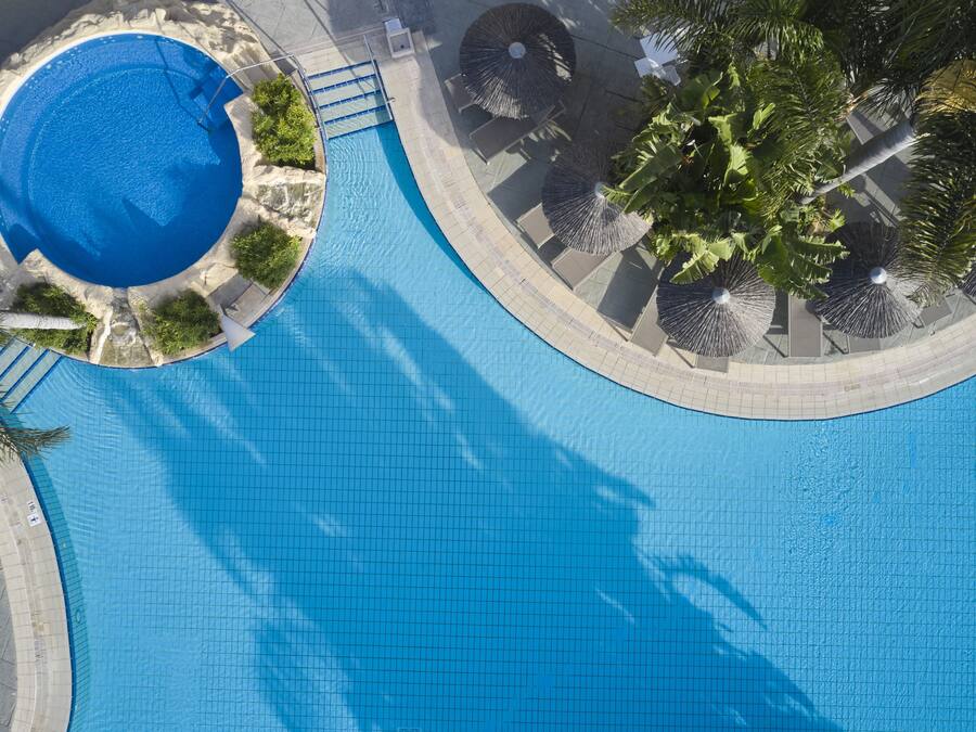 Una piscina grande y cristalina de color azul con un borde de baldosas y palmeras cercanas.