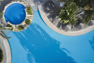 Una piscina grande y cristalina de color azul con un borde de baldosas y palmeras cercanas.