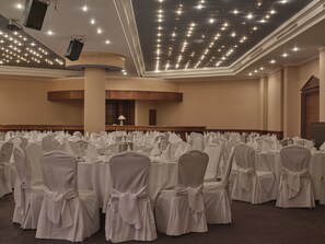A banquet hall with round tables, chairs with white covers, and a stage with a podium.