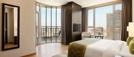 A hotel room with a large bed, a TV, a balcony with a chair, and a city view.