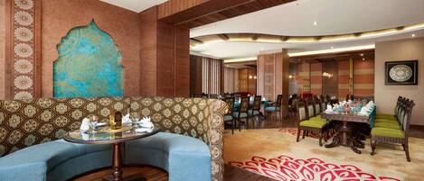 A modern hotel lobby with a curved sofa, a round table, and a dining area with chairs.