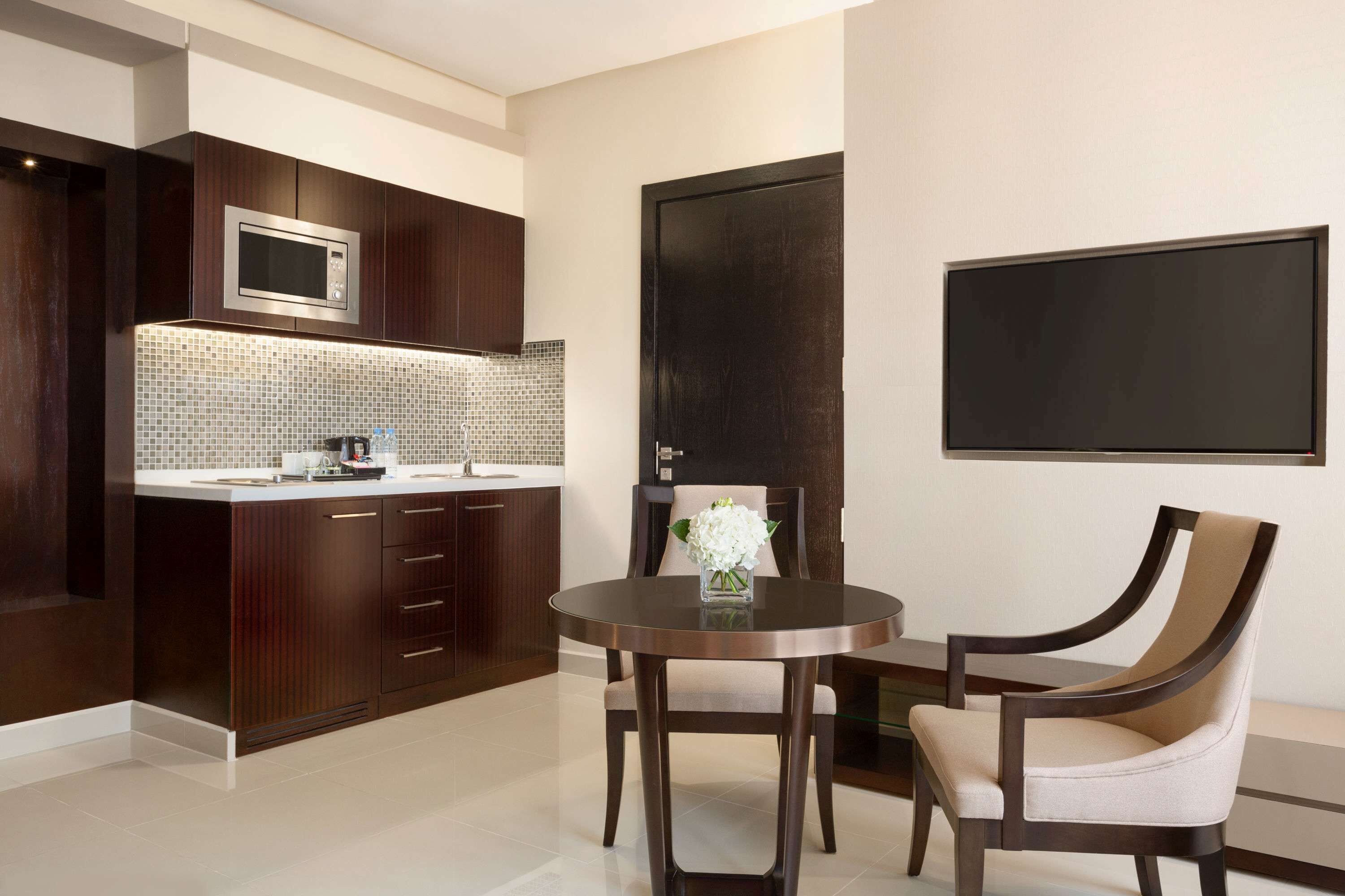 A modern kitchen with dark wooden cabinets, a stainless steel microwave, and a tiled backsplash.