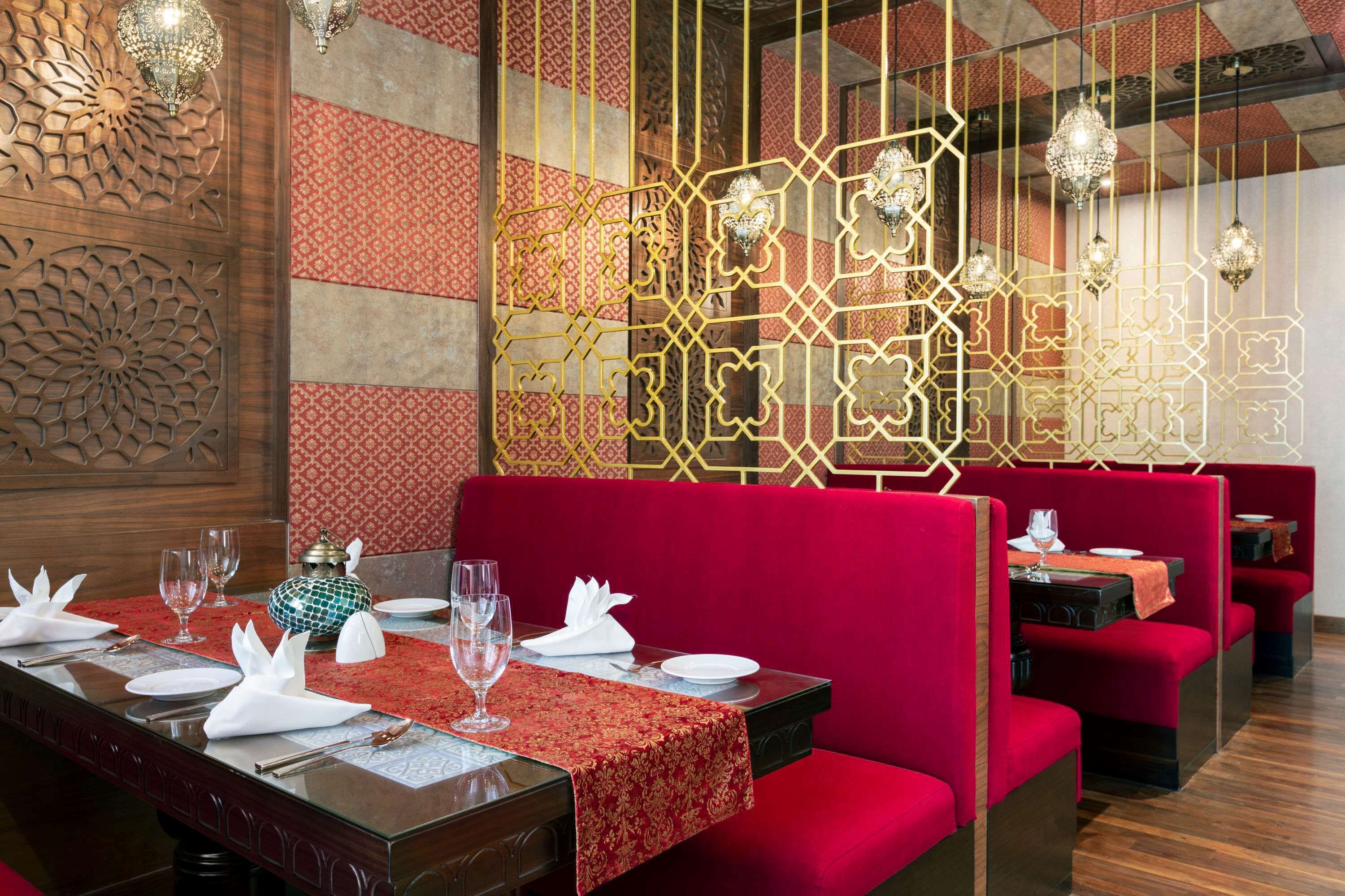 A restaurant with red upholstered booths, a patterned wall, and a wooden panel with intricate carvings.