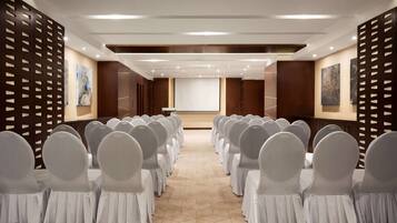 A conference room with rows of chairs, a projector screen, and artwork on the walls.