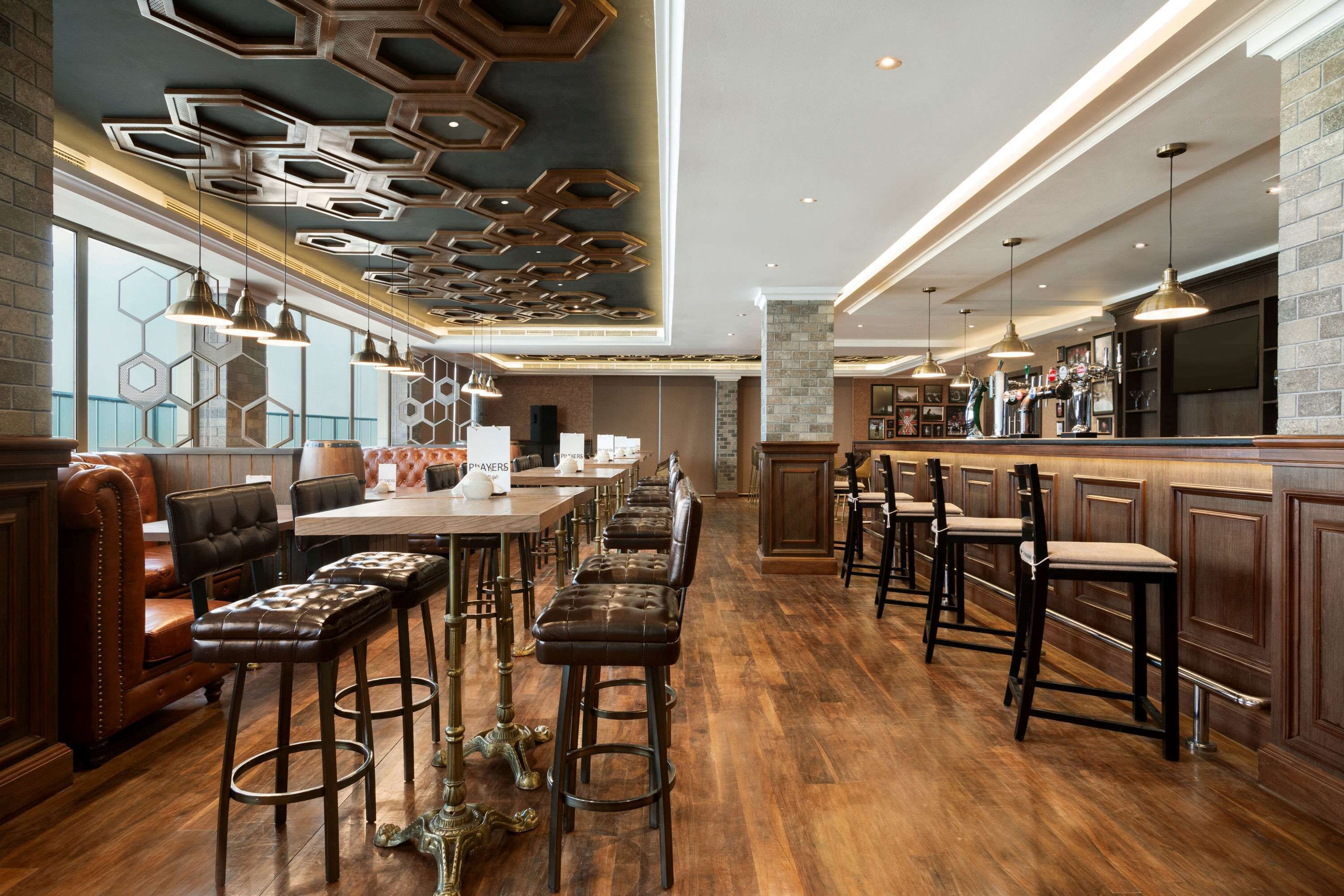 A modern bar area with wooden flooring, leather barstools, and hexagonal ceiling designs.