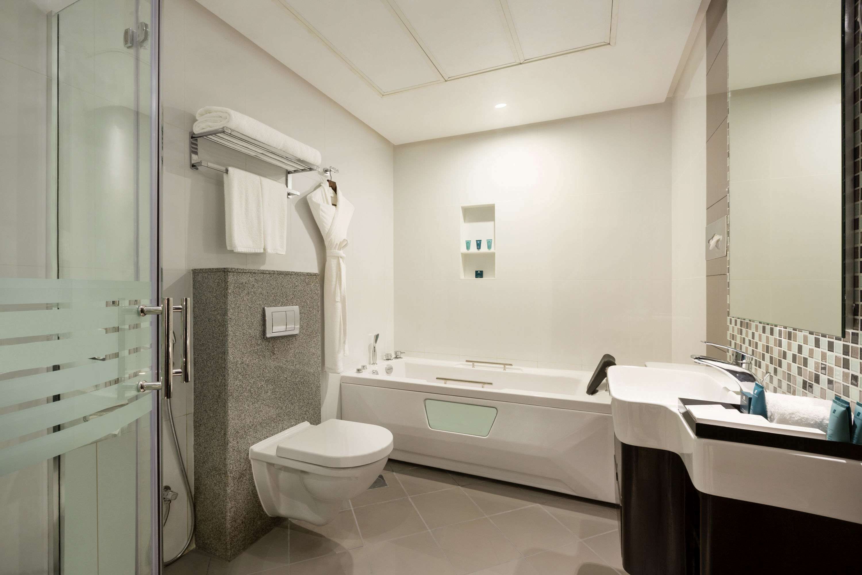 Un baño moderno con cabina de ducha de vidrio, inodoro blanco, bañera independiente y tocador con espejo.