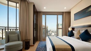 Camera d'albergo con un letto grande, una poltrona, una TV e vista sulla città.