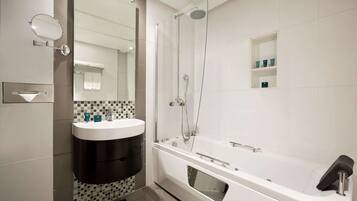Un baño moderno con un lavabo blanco, ducha con cerramiento de vidrio y estante empotrado con artículos de aseo.