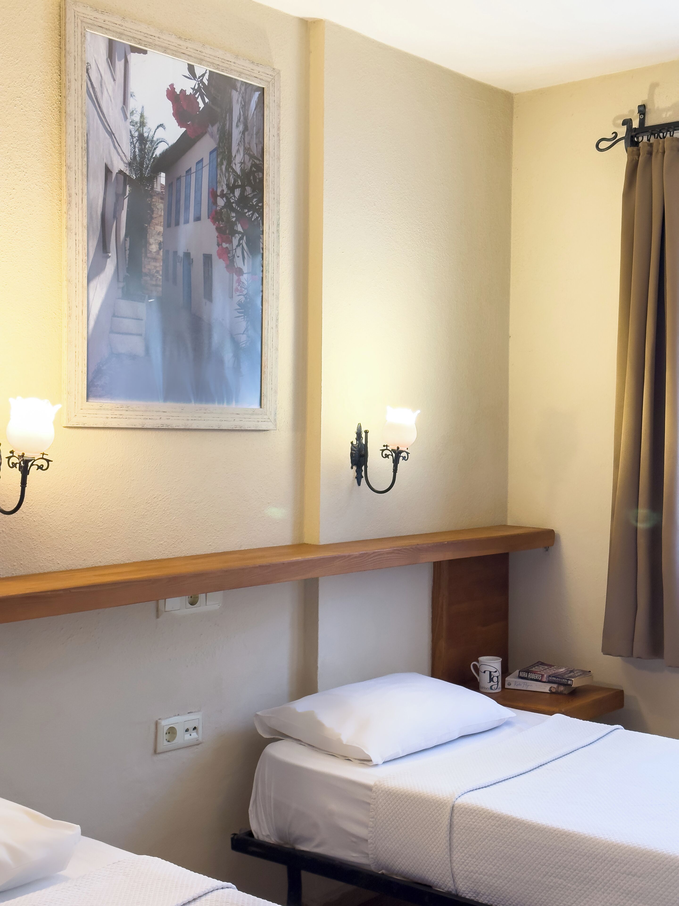 A hotel room with two beds, a painting on the wall, a shelf with a lamp, and a window with curtains.
