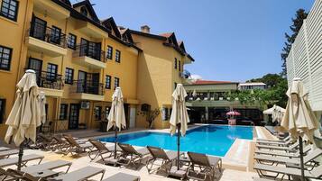 A pool area with lounge chairs and umbrellas, a yellow building with balconies, and a clear blue sky.