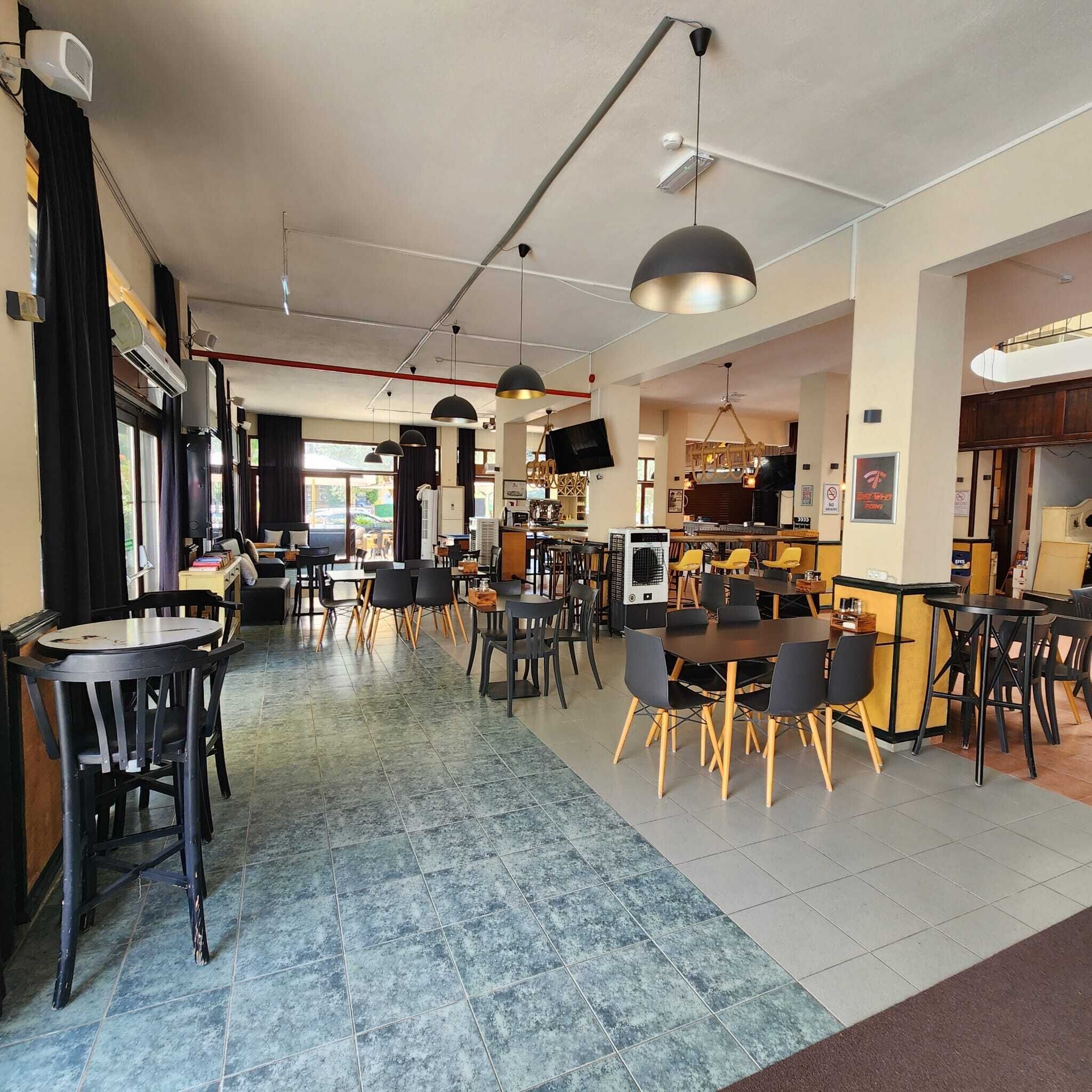 A modern cafe with multiple seating areas, including tables and chairs, and a visible kitchen area.
