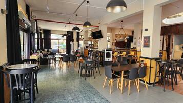 A modern cafe with multiple seating areas, including tables and chairs, and a visible kitchen area.
