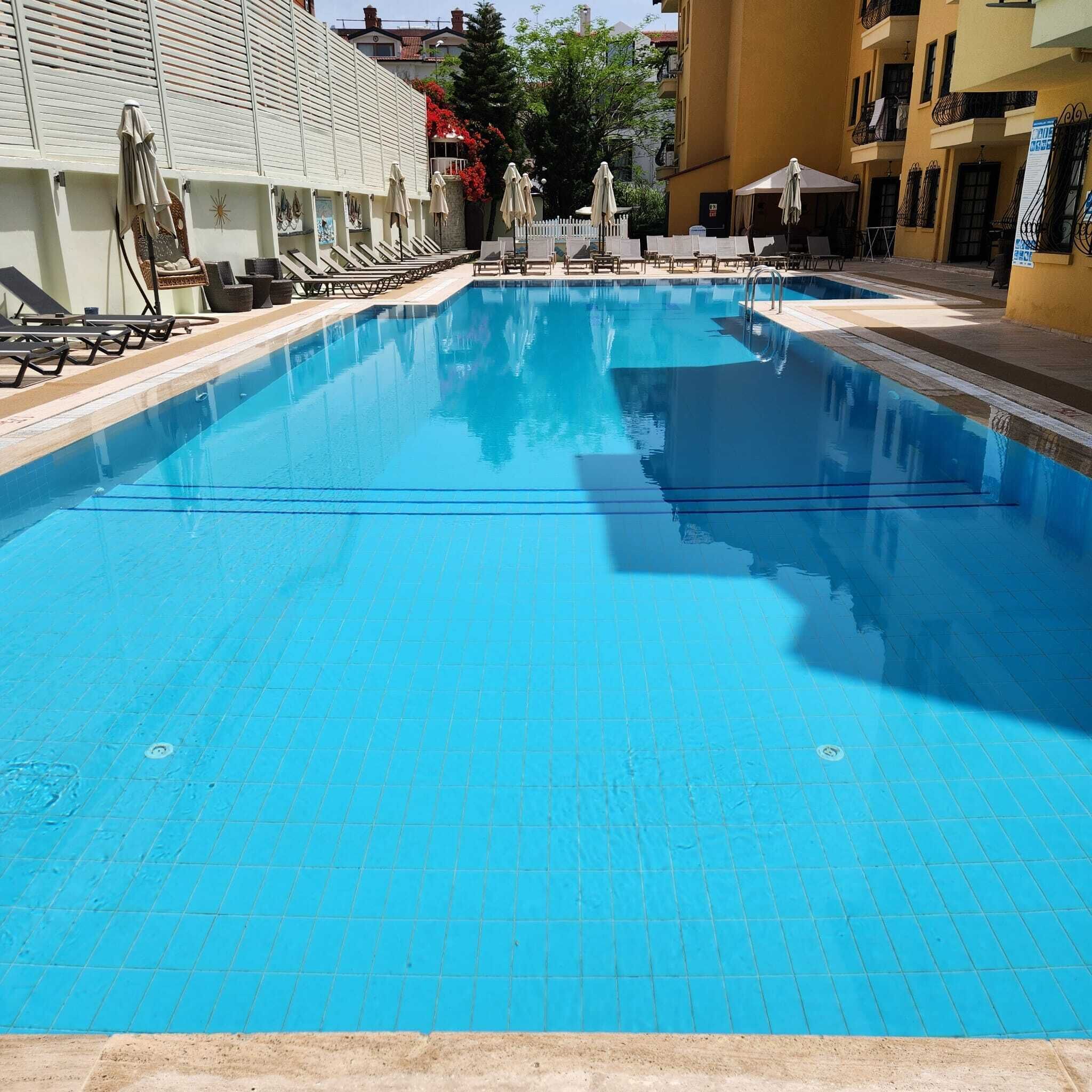 A swimming pool with lounge chairs and umbrellas, surrounded by buildings.