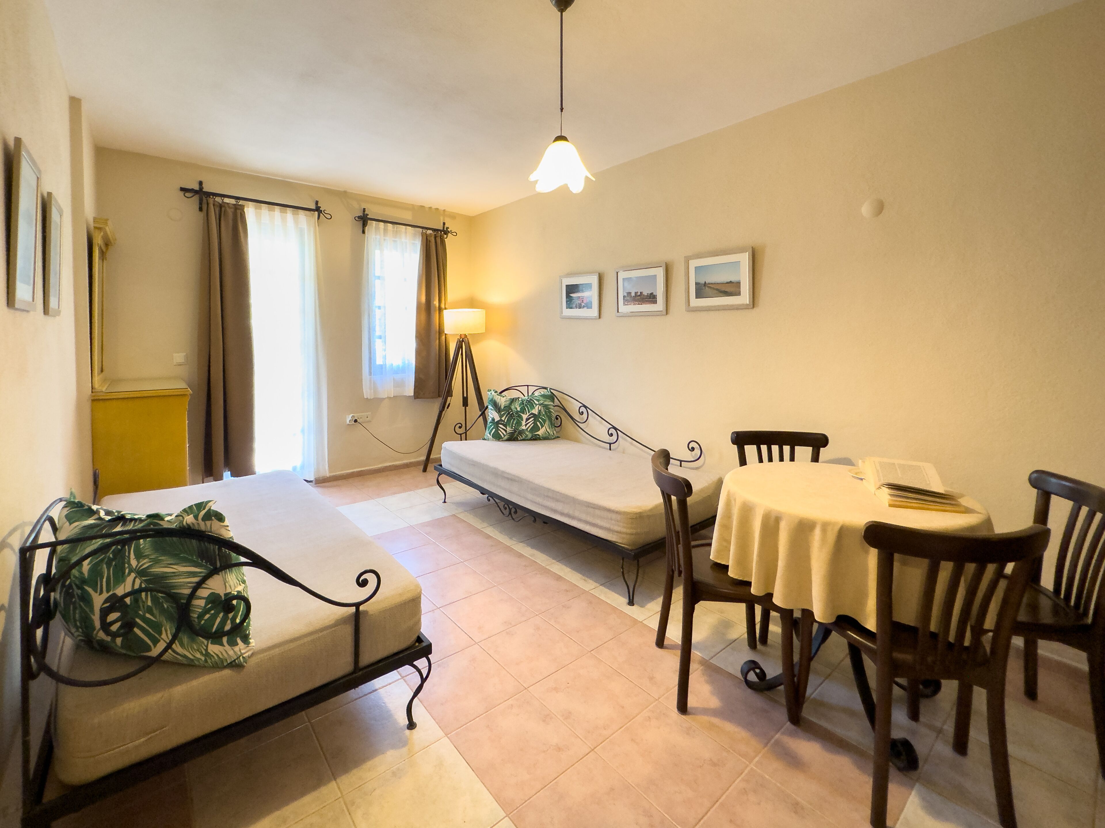 A room with a bed, a small table with chairs, a lamp, and framed pictures on the wall.