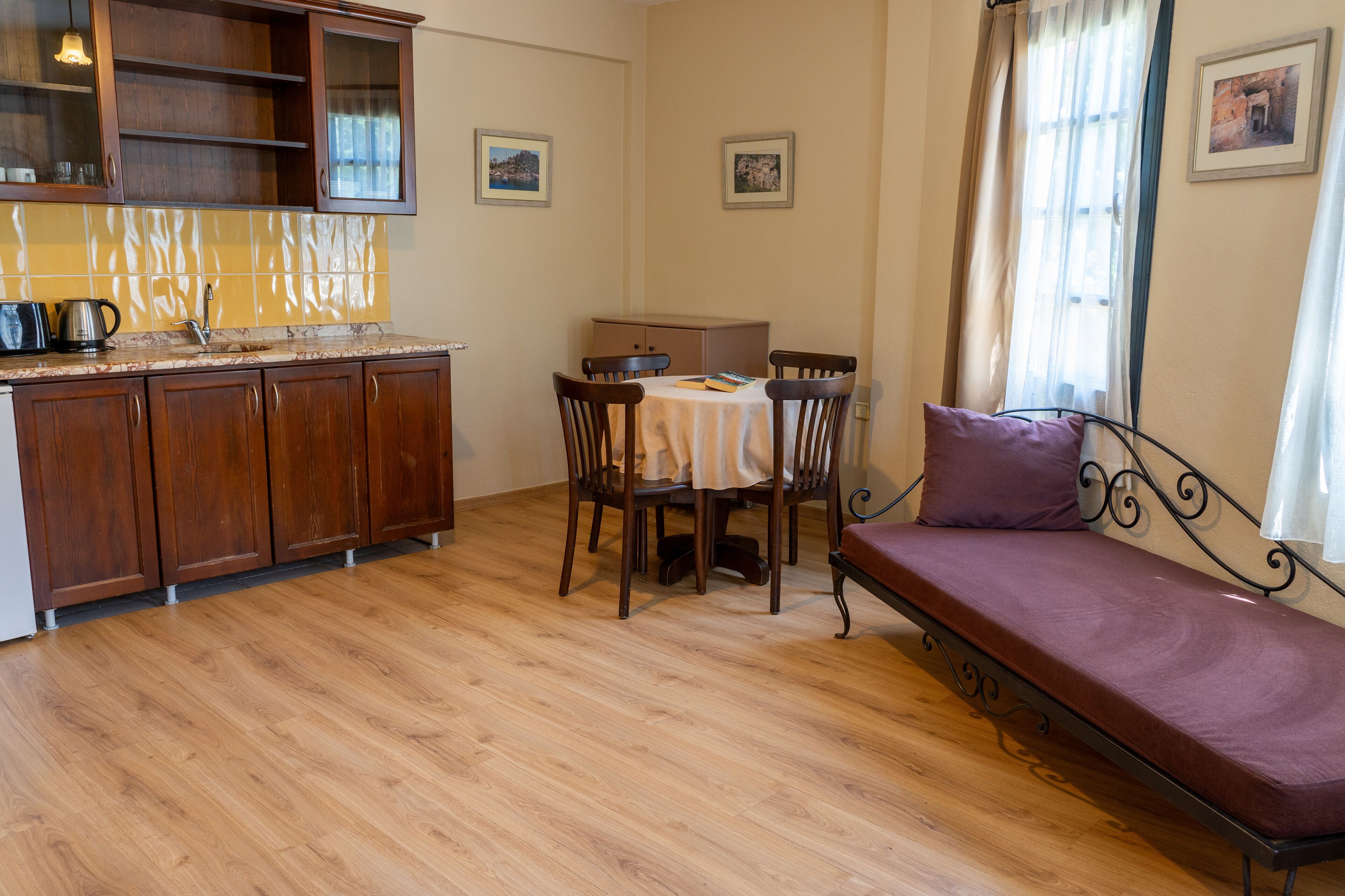 Een knus woongedeelte met kitchenette, een eethoek met tafel en stoelen, en een bank met kussen.