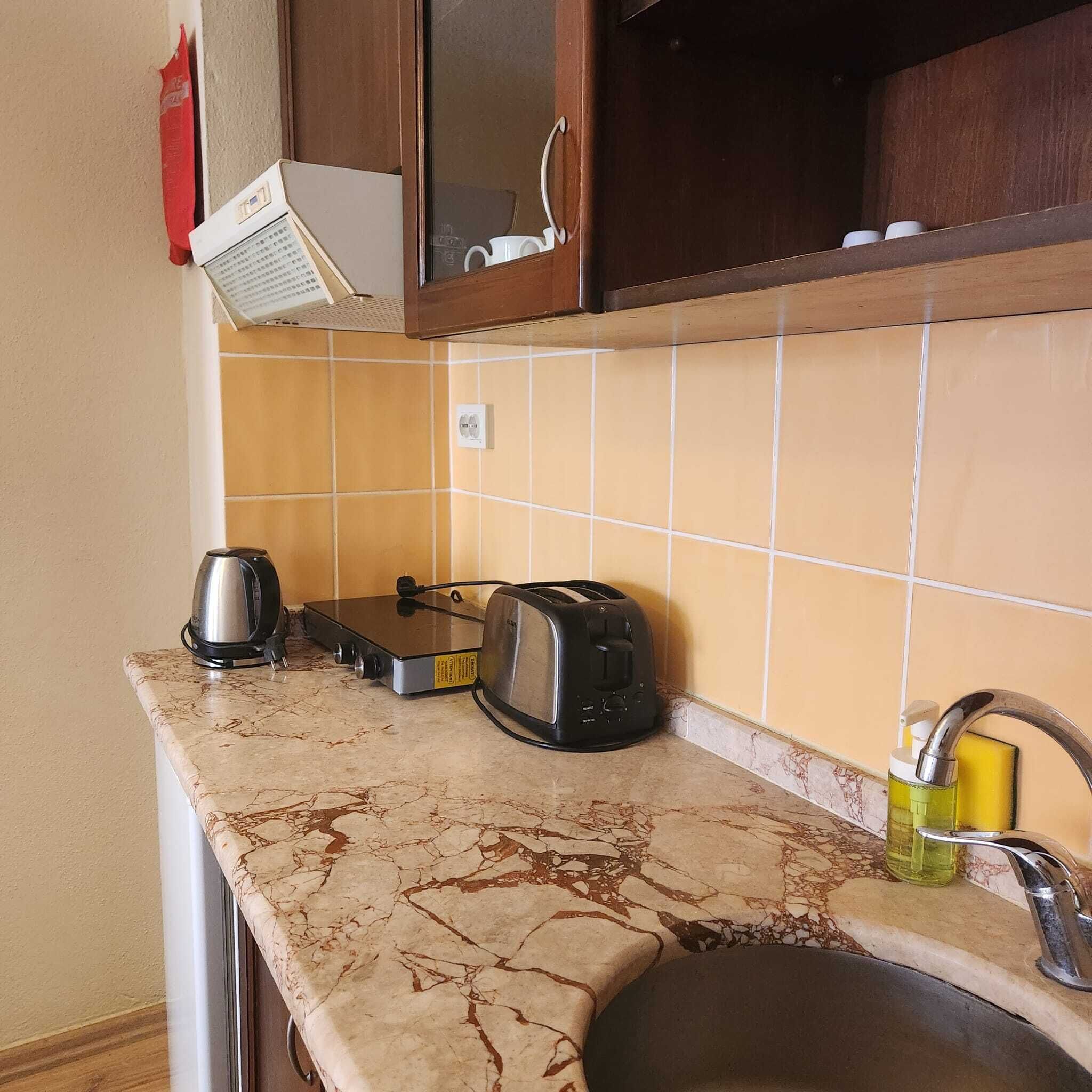 Una cocina con encimera de mármol, un tostador, un hervidor y un lavabo con grifo.