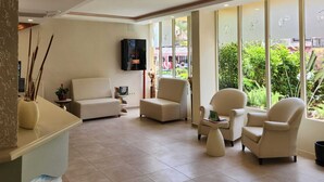 A spacious lobby with a sofa, armchairs, a TV, and large windows offering a view of greenery. - T & G Apartments (Marmaris)