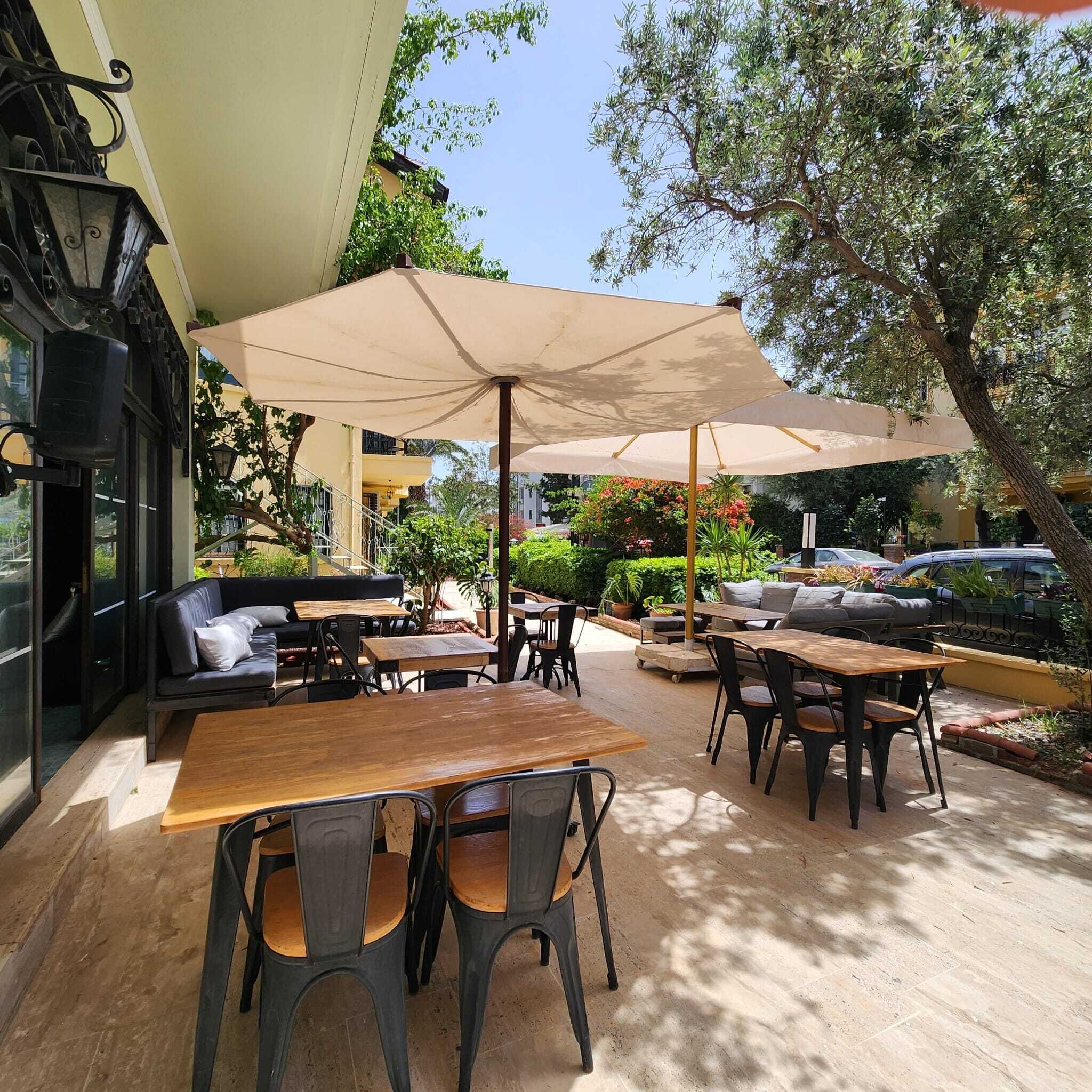 An outdoor patio with tables and chairs, a large umbrella, and a staircase leading to an upper level.