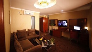 A living room with a sofa, a coffee table with fruits and a laptop, a TV, and a desk with a computer.